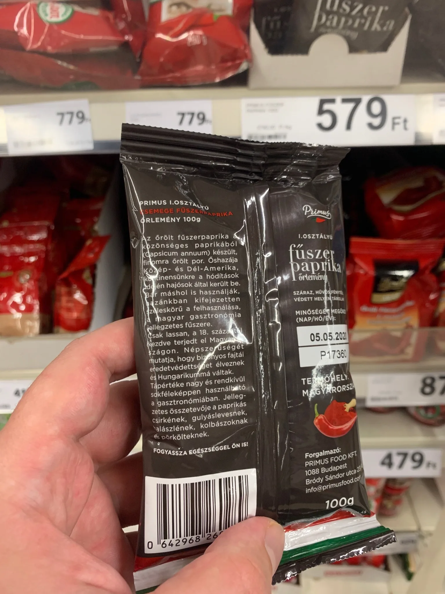 Fekete csomagolású őrölt fűszerpaprika kézben, piros paprikás termékek polca előtt