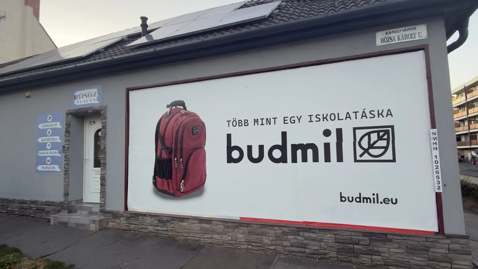 Budmil óriásplakát piros hátizsákkal, Több mint egy iskolatáska felirattal, logóval és webcímmel