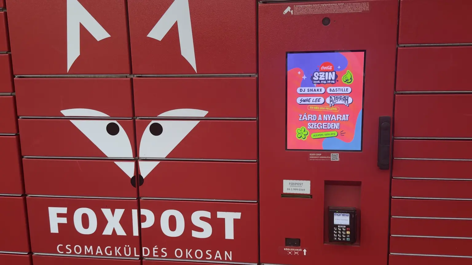 Vörös FOXPOST csomagautomata beépített digitális kijelzőjén Coca-Cola Sziget 2026 reklám