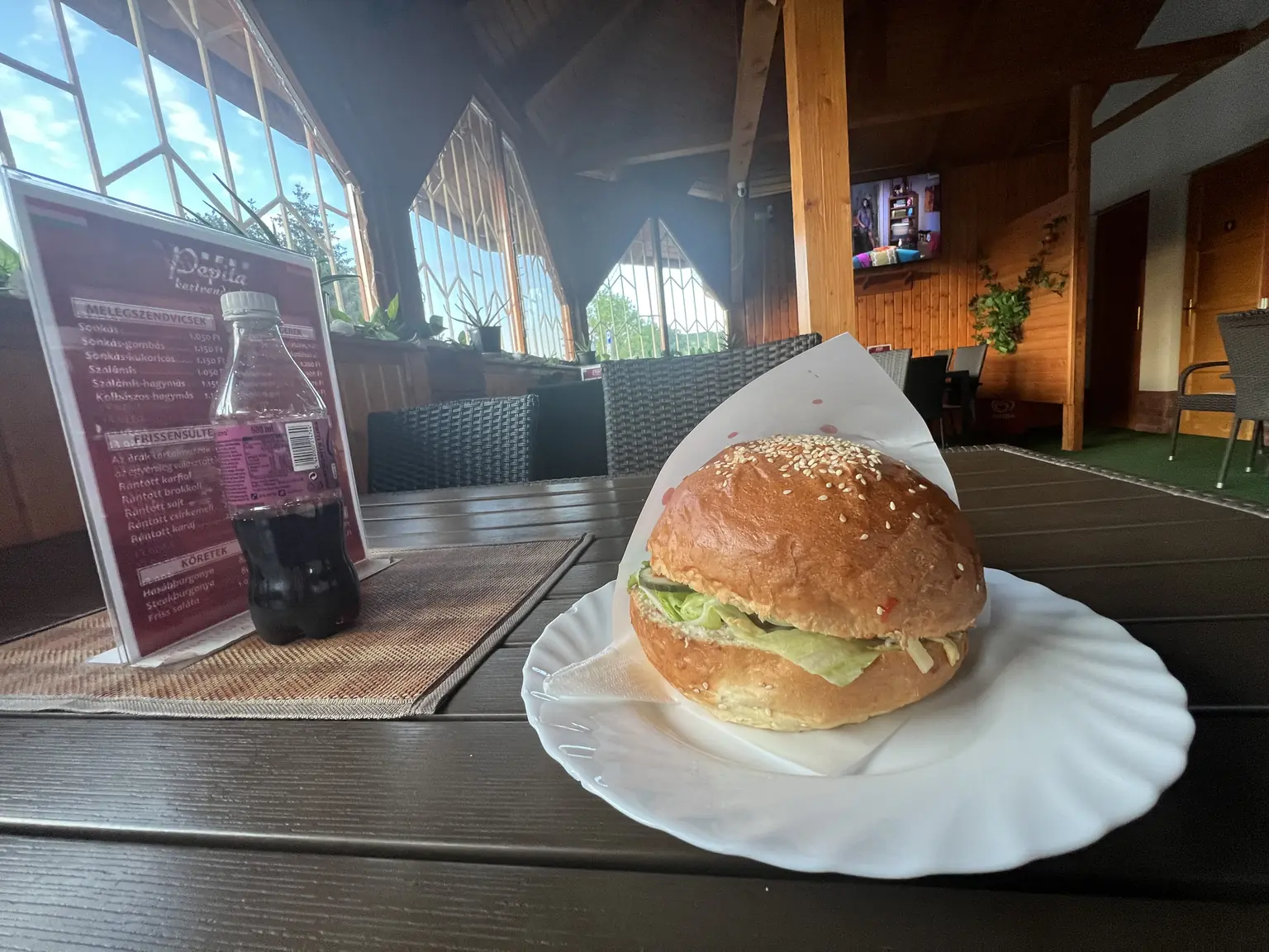 Hamburger tányéron egy vendéglátóhely asztalán, mellette ital és laminált ételárlista