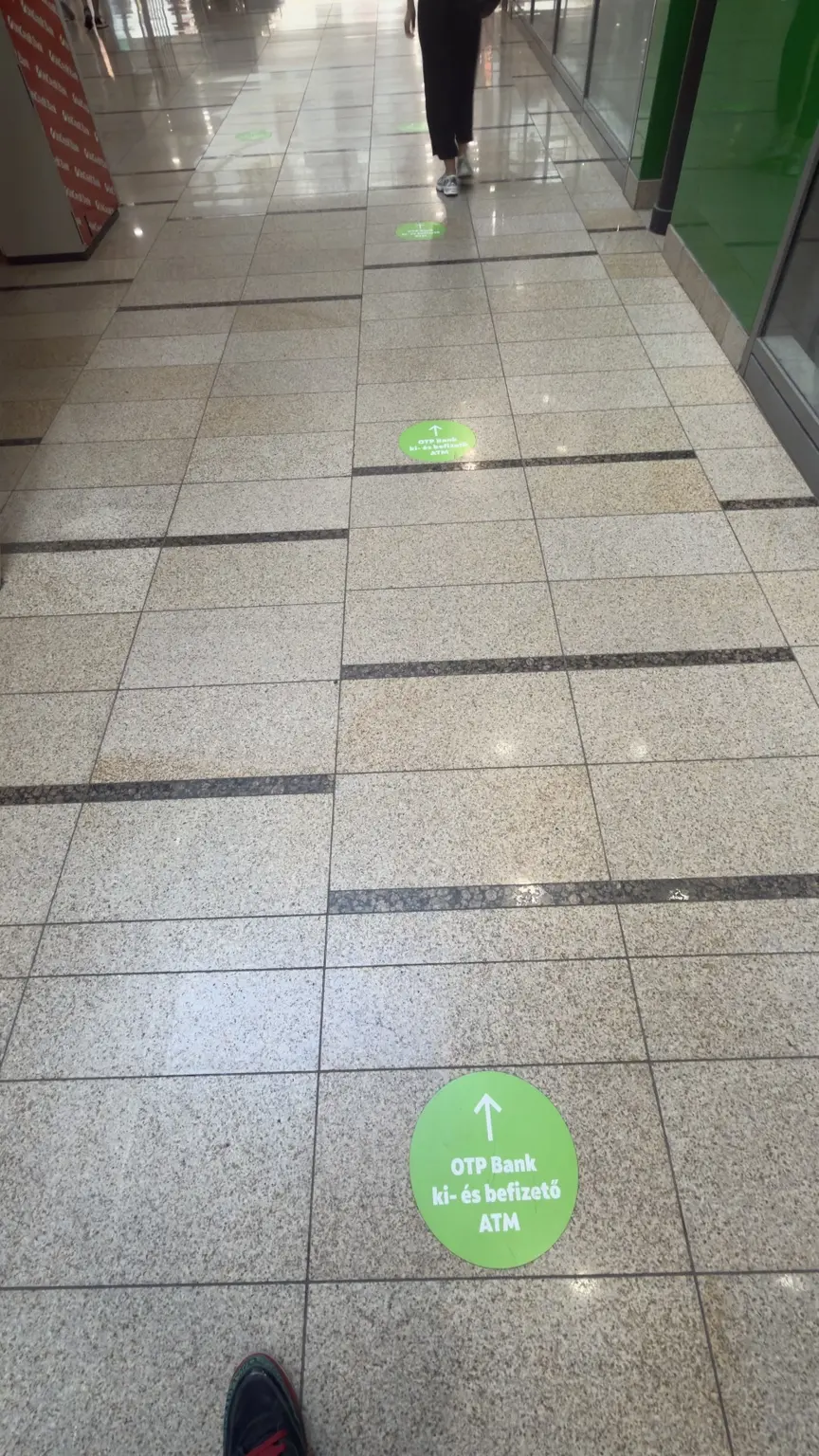 Bevásárlóközpont folyosóján ismétlődő zöld OTP Bank padlómatricák mutatják az ATM irányát