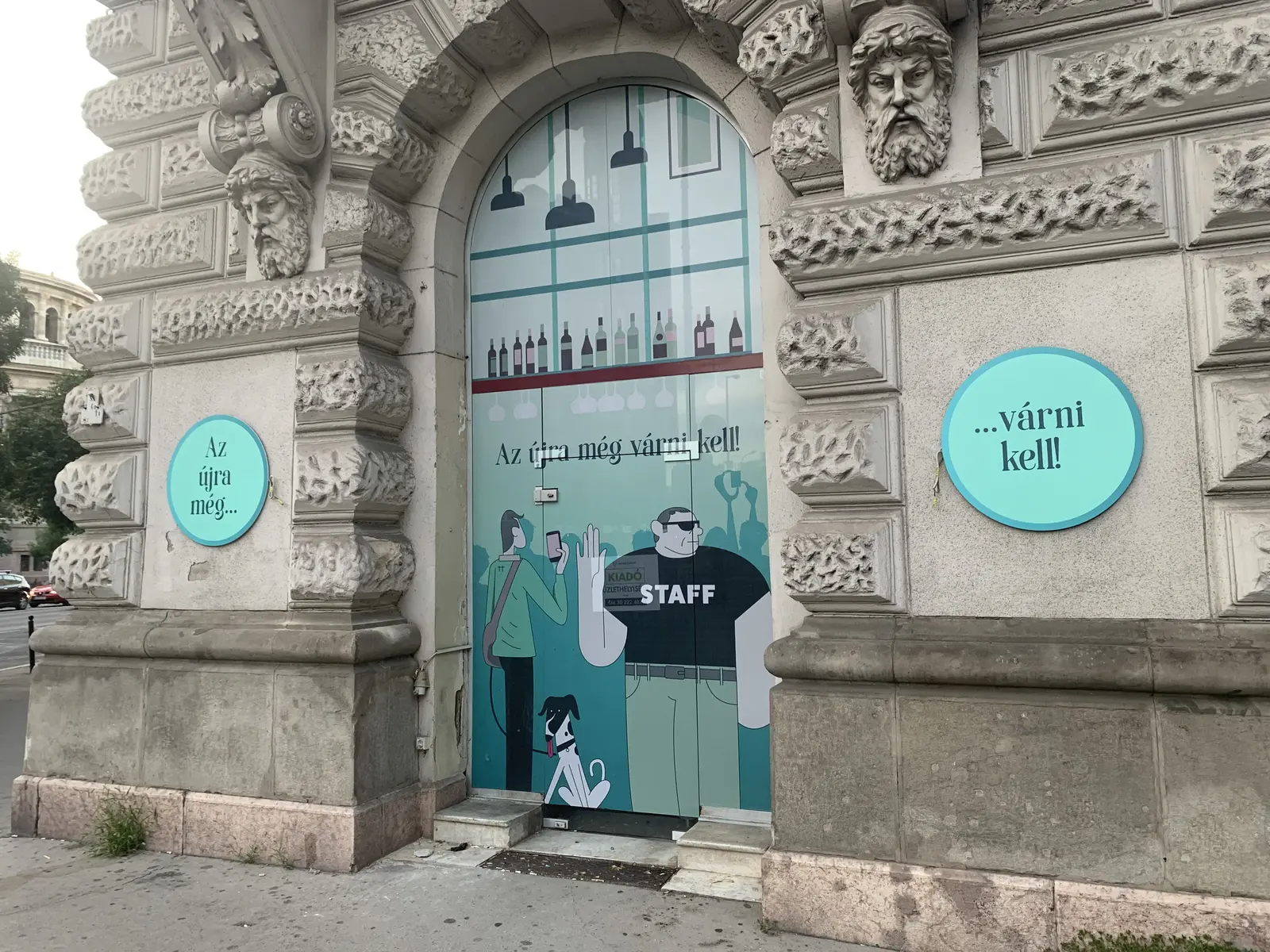 Díszes budapesti üzletportál türkiz fóliával és Az újra még várni kell felirattal egy kiadó üzlethelyiségen