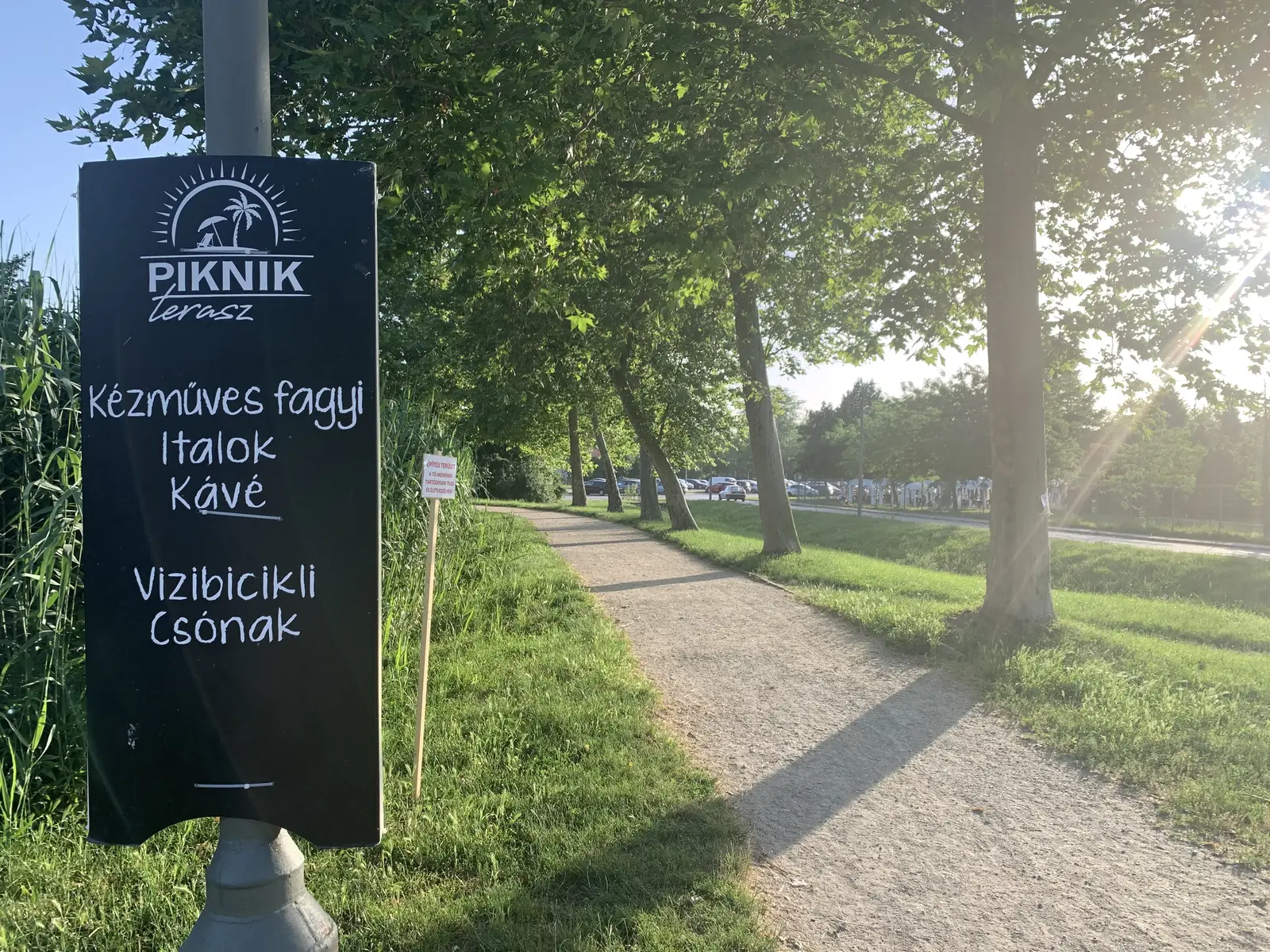 Fekete Piknik terasz tábla kézműves fagyi, italok, kávé, vízibicikli és csónak kézzel írt kínálatával egy gyalogút mellett
