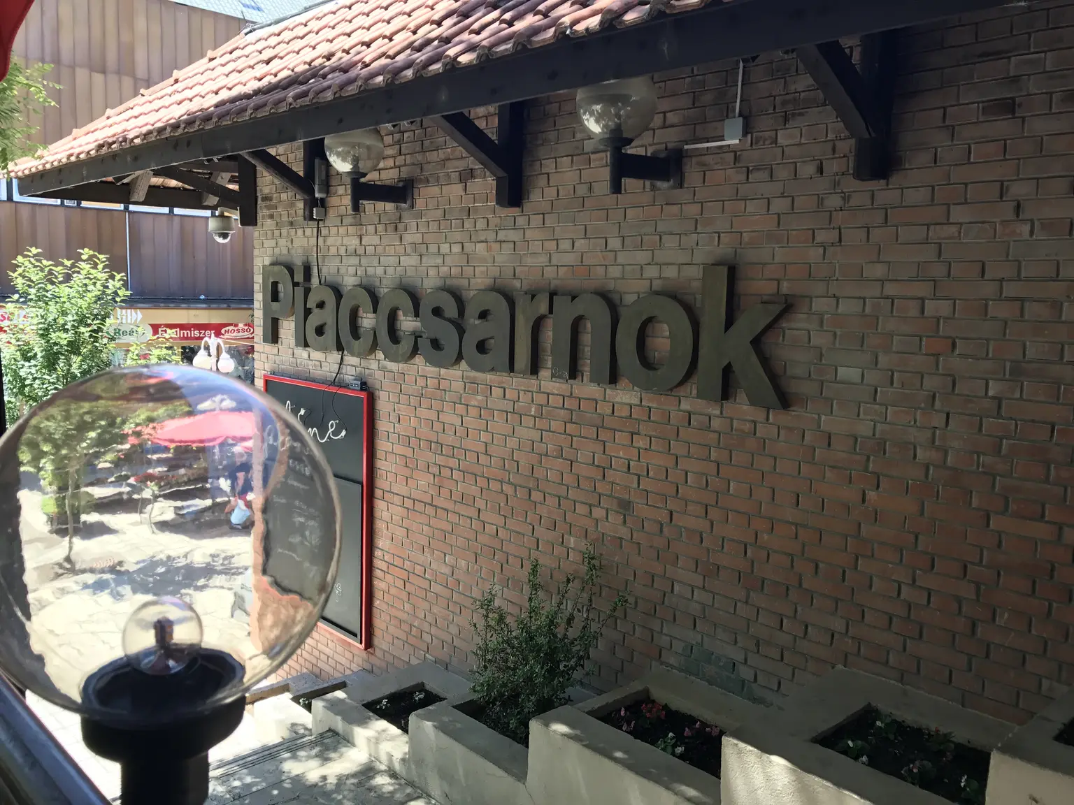 Piaccsarnok felirat nagyméretű térbetűkkel egy téglafalon, a bejárati környezetben