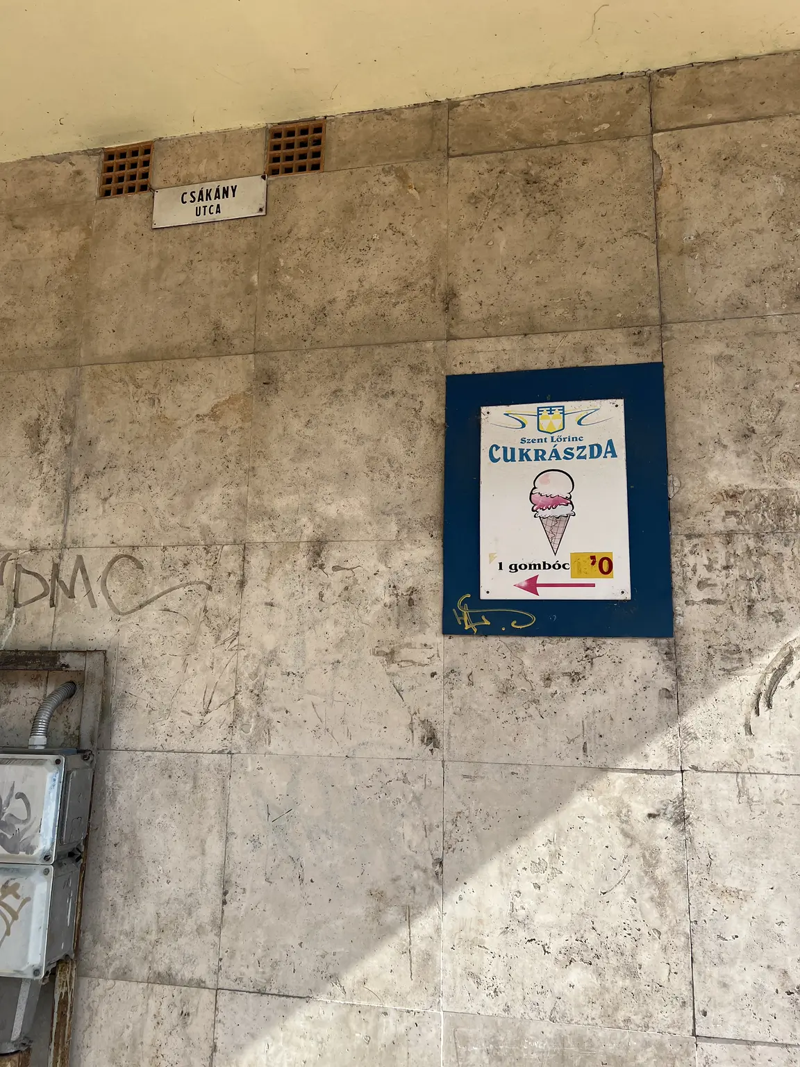 Szent Lőrinc Cukrászda balra mutató fagylalttáblája egy egri aluljáró kőfalán