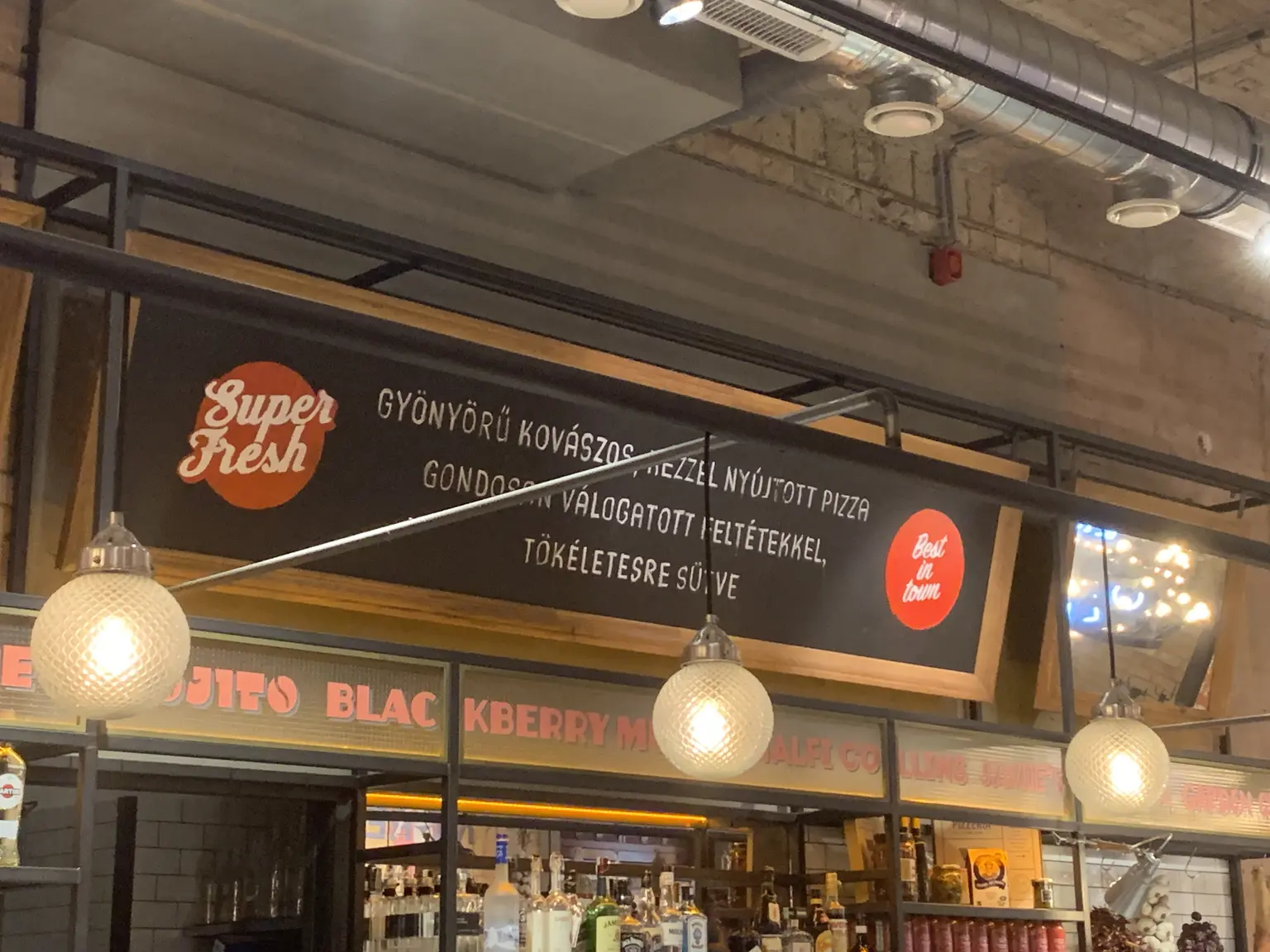 Éttermi pult fölötti fekete falpanel frissességet és gondos pizzakészítést hangsúlyozó feliratokkal Budapesten