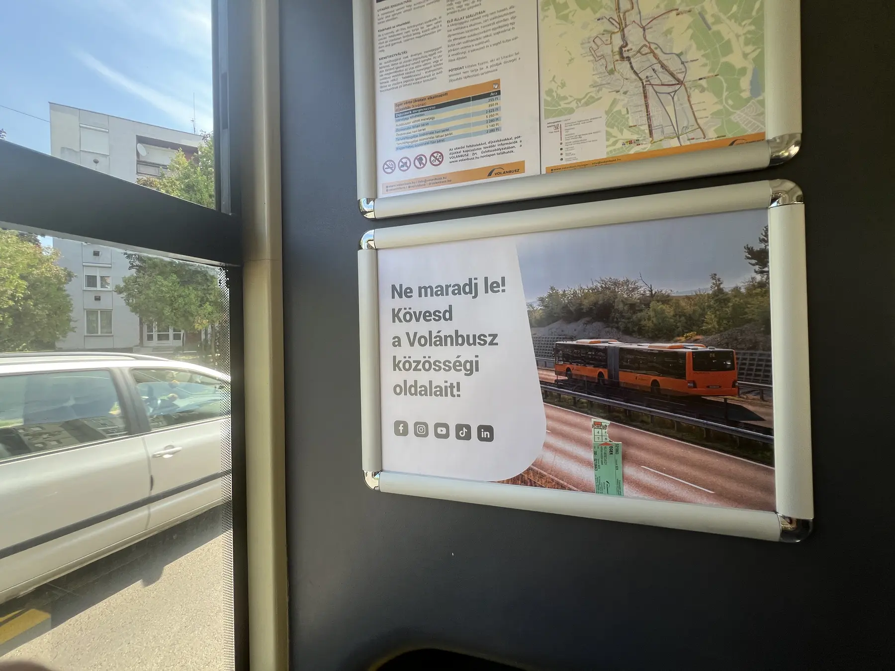 Volánbusz közösségi oldalait hirdető fedélzeti plakát az autóbusz ablakánál