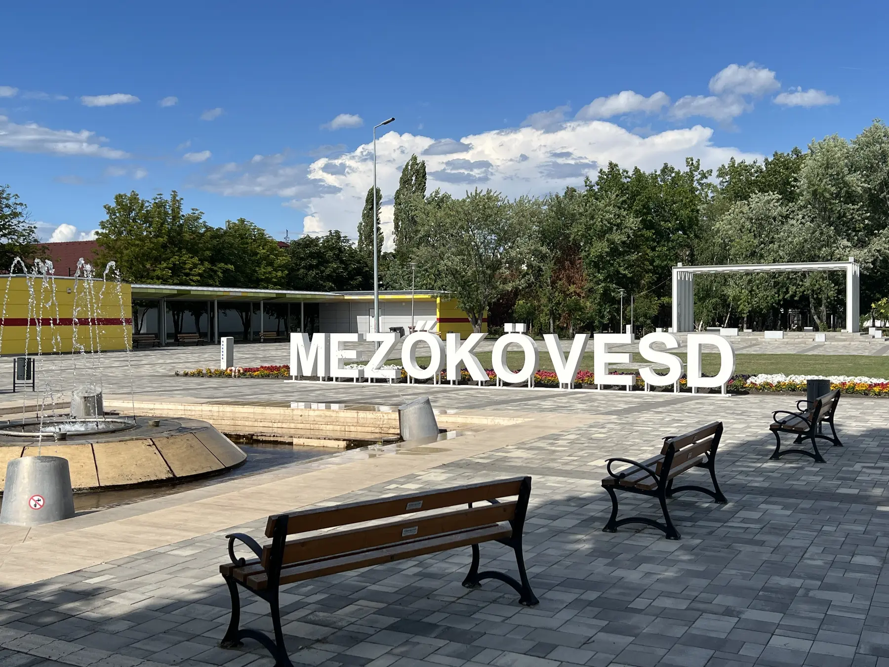 Nagyméretű fehér MEZŐKÖVESD térbetű szökőkút és park előtt