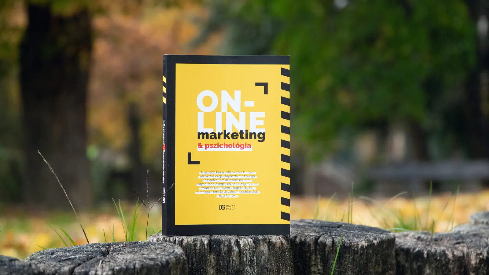 Online marketing és pszichológia könyv egy farönkön, parkos háttérrel