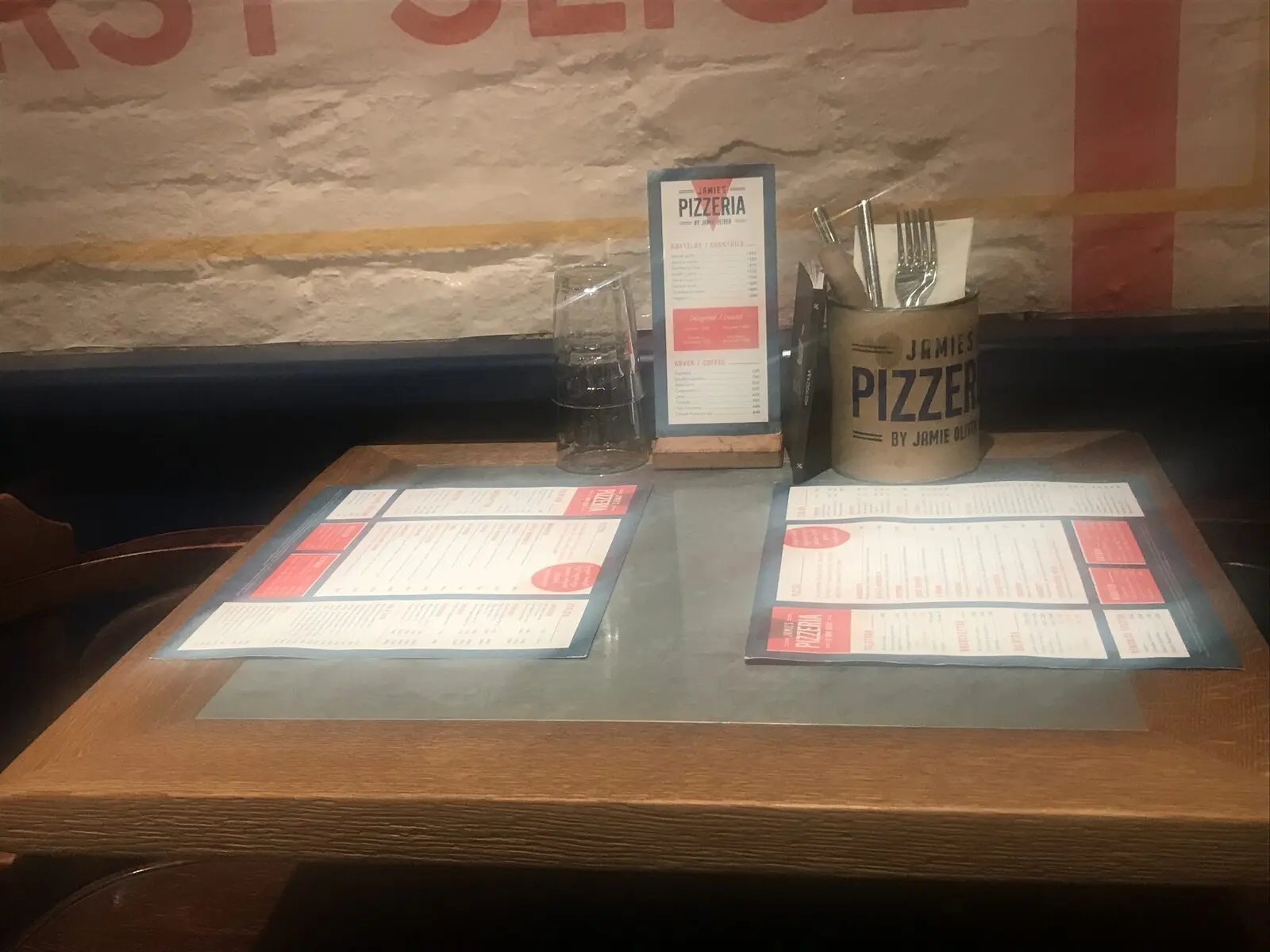 Jamie’s Pizzeria éttermi asztal két étlappal, álló itallappal, márkázott evőeszköztartóval és feliratos fallal