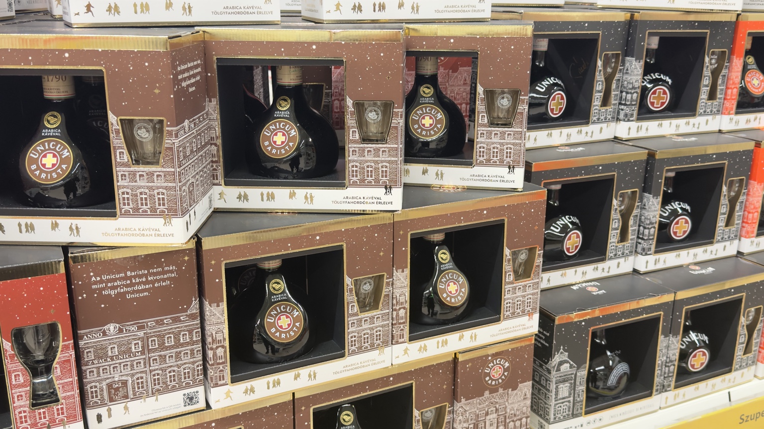 Unicum és Unicum Barista ajándékdobozok bolti sora, az ablakokban üveggel és pohárral, barna-fekete és arany csomagolással.